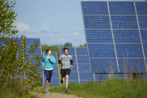 学生慢跑跑道的跑步通过在佛蒙特州米德伯里学院郊区的太阳能电池板。