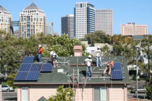 工人们在奥克兰市中心附近的一所房子上安装太阳能电池板，这是一项利用加州限额交易拍卖收入的计划。