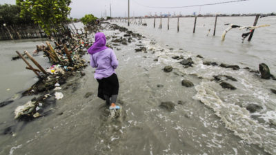 女人走过一个破堤造成海平面上升在爪哇中部,印尼在2018年2月。