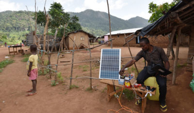 一名男子使用太阳能电池板充电在象牙海岸的遥控村庄中的手机和其他电气设备，缺乏电力。