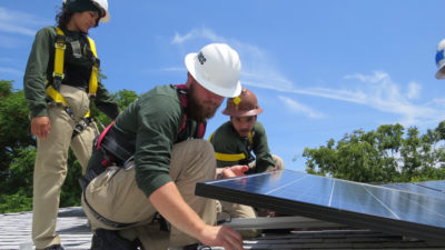 工人安装一个太阳能电力系统在萨克拉门托的残疾人靠固定收入生活的人。该系统将提供一个估计22800美元的能源节约。