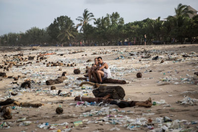 假期坐在巴厘岛顶级旅游目的地之一Kuta Beach散落的塑料废物中。