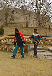 甘西省农村地区的儿童从学校里从一口井中收集水。